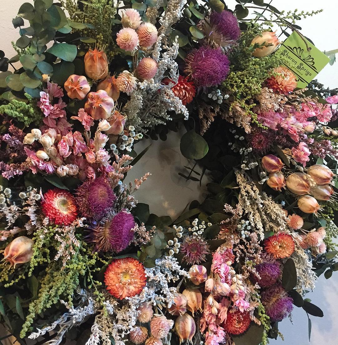 A colorful spring/summer wreath with various dried flowers, ranging from pink hues, to burgundy, to green, and yellow.