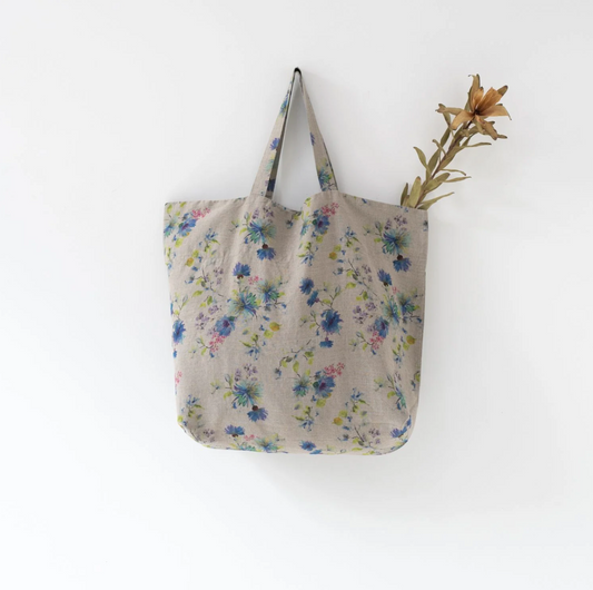 A Linen Tales Floral Linen Bag with blue floral designs and a dried lily flower stem sticking out from the top.