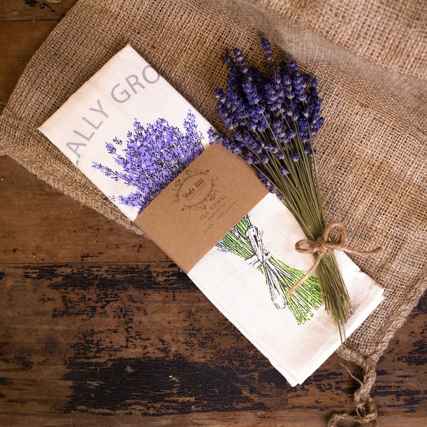 "Locally Grown" Lavender Tea Towel displayed on a burlap covered table. Made by Slate Hill Farm in Sharon Springs, NY.
