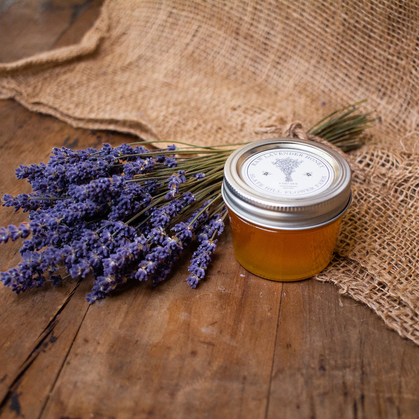 Small glass jar of lavender honey next to a lavender bundle on burlap.