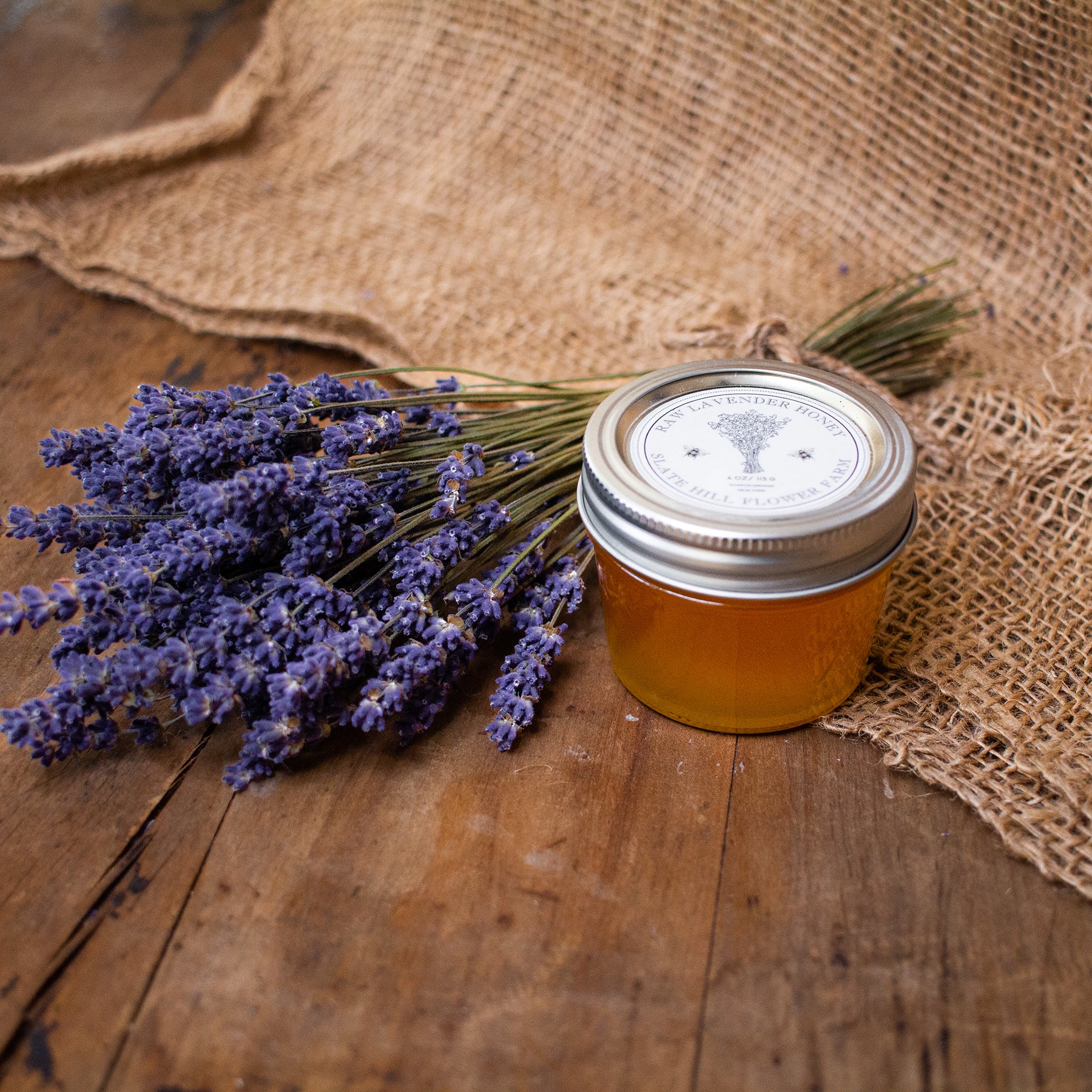Small glass jar of lavender honey next to a lavender bundle on burlap.