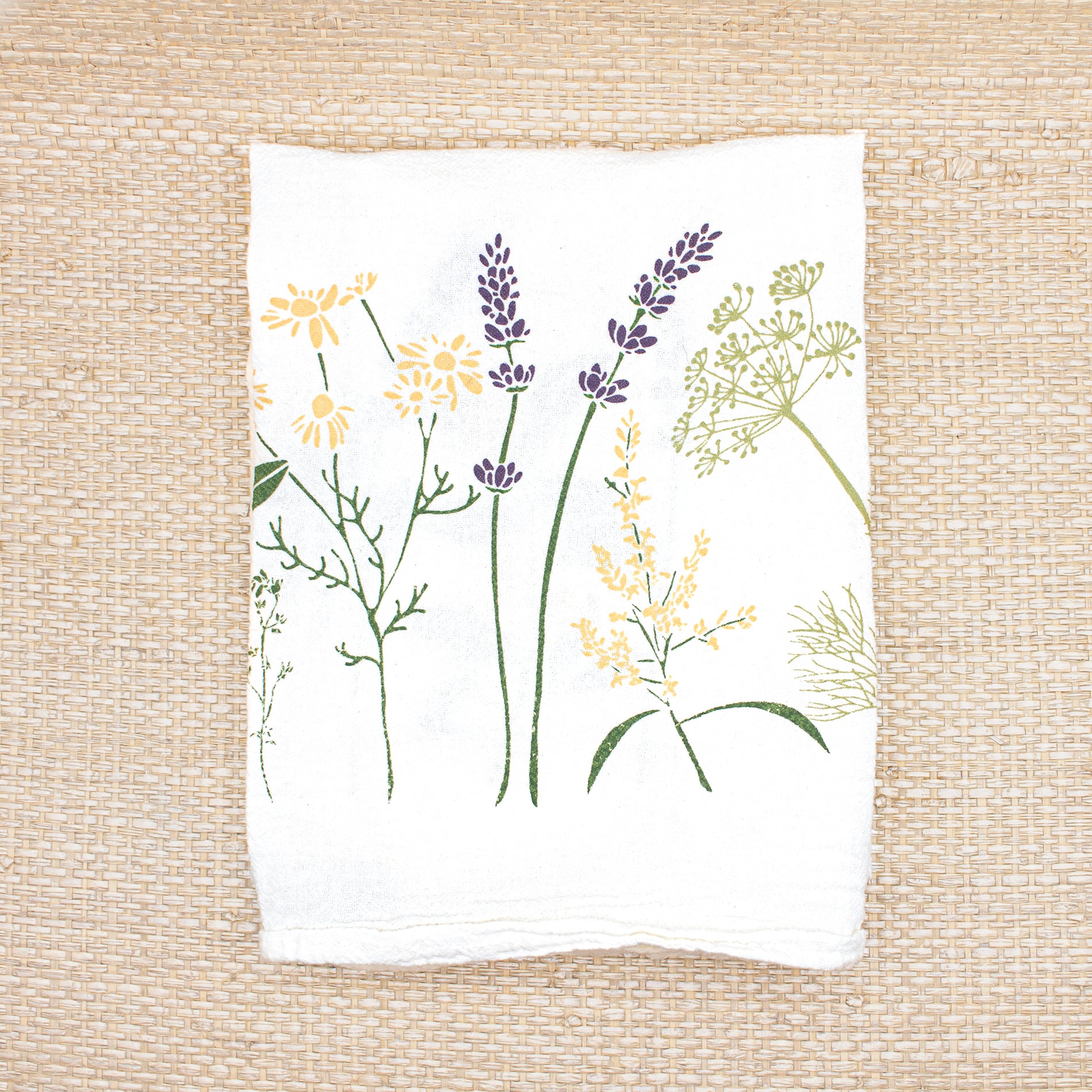 A folded June & December branded white tea towel with herb and flower designs.