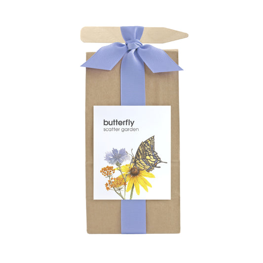 A long brown bag filled with scatter garden seeds. Wrapped with a periwinkle ribbon that also holds a garden marking stick. Label on the front has a butterfly & flowers graphic with text that reads "Butterfly Scatter Garden".