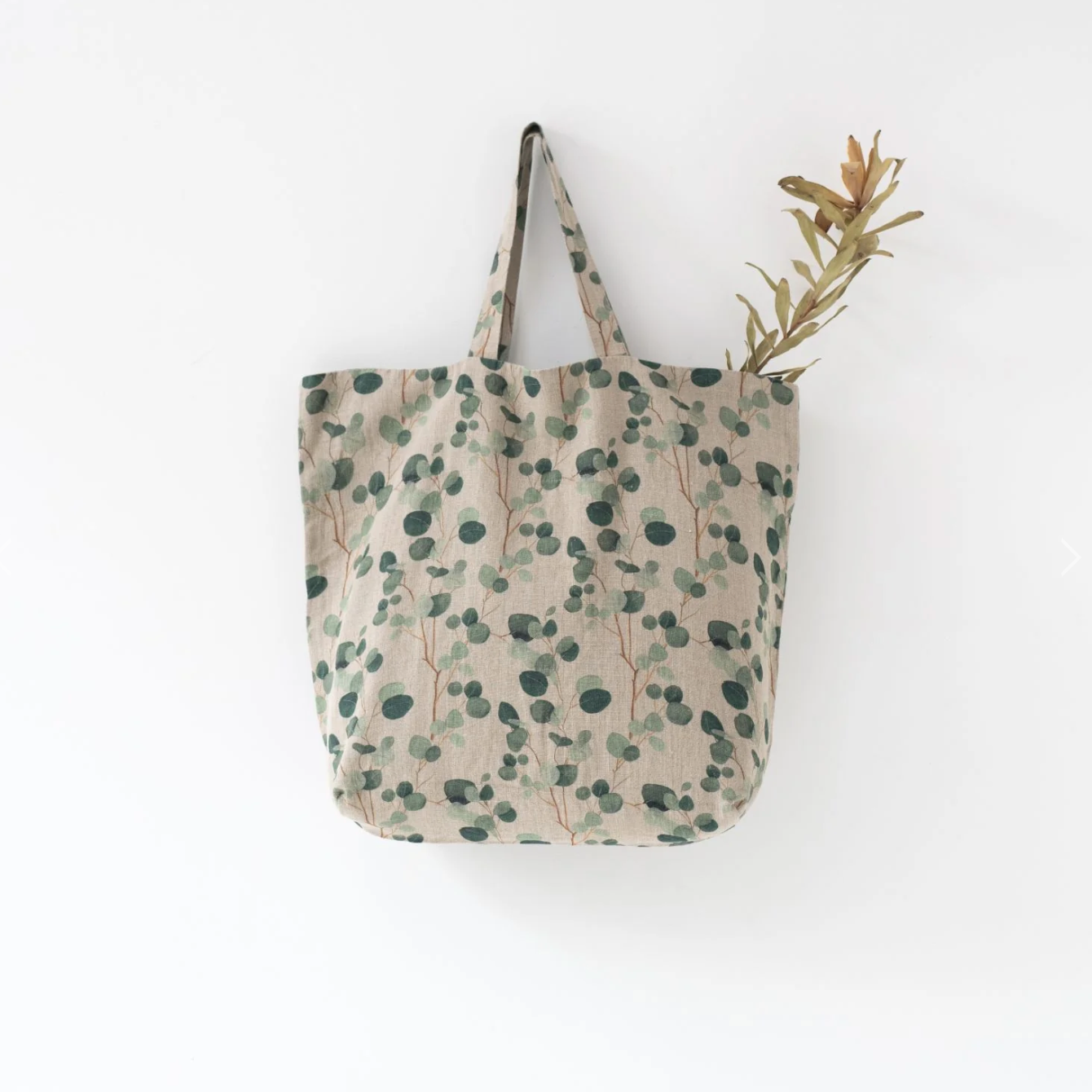 A Linen Tales Floral Linen Bag with eucalyptus designs and a lily flower stem sticking out from the top.