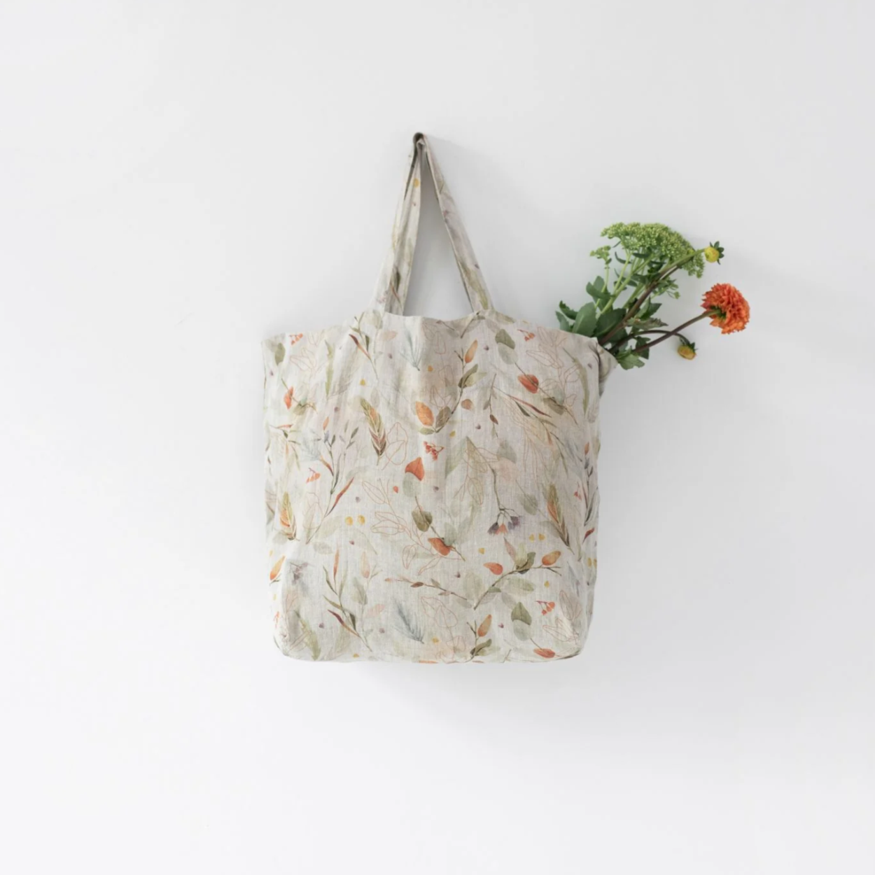 A Linen Tales Floral Linen Bag with earthy floral & leaf designs and a flower bouquet sticking out from the top.